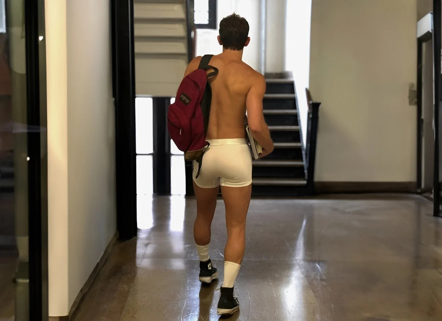 Man wearing ALPHX Boxer Brief in Frost White, confidently walking down a brightly lit school hallway.